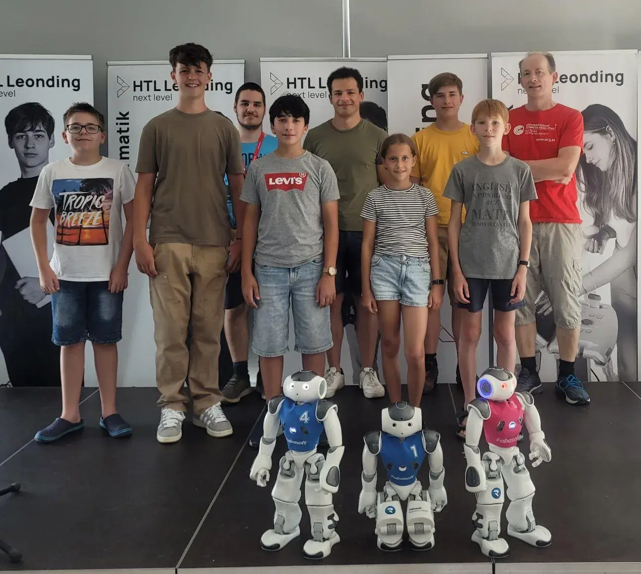 Gruppenfoto vom Sommercamp in Leonding mit den Trainern und Teilnehmer*innen sowie 3 Robotern