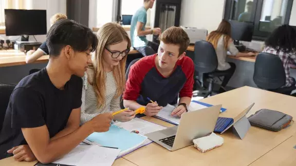 Zwei Schüler und eine Schülerin sitzen vor einem Laptop