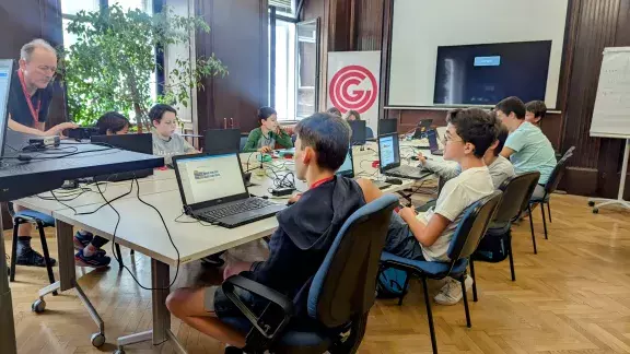 Informatik Fun Gruppe des OCG Sommercamps: Jugendliche vor Laptops sitzend, OCG Roll-up mit Logo im Hintergrund.