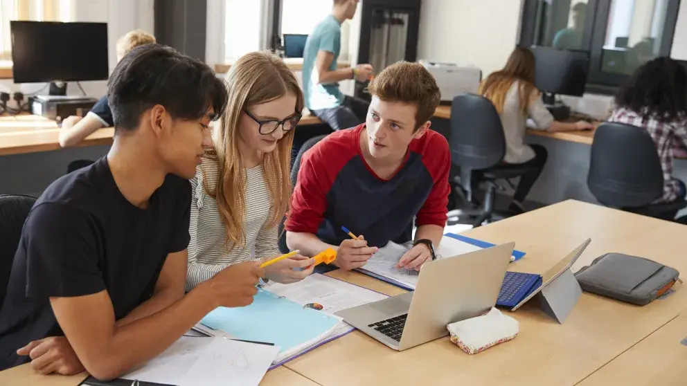 Zwei Schüler und eine Schülerin sitzen vor einem Laptop